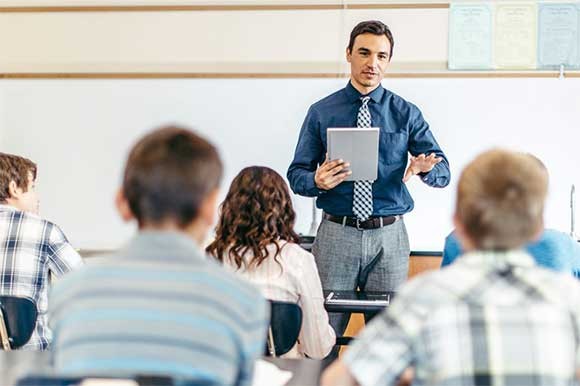 Een docent staat voor de klas met een tablet