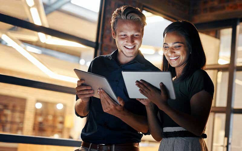 Een mannelijke en vrouwlijke collega gebruiken lachend een tablet
