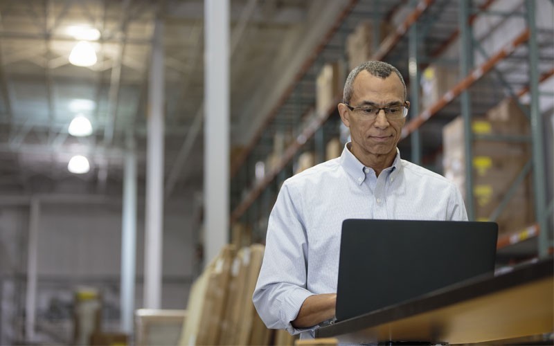 Zakenman die op laptop werkt in het magazijn