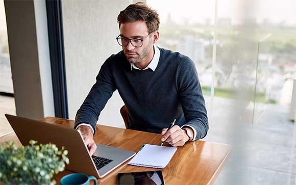 Man die op een laptop werkt met een tablet op de tafel.